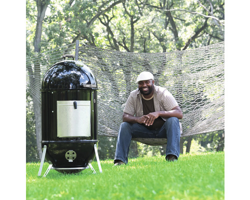 Vertikaler Holzkohlegrill neben einer Person auf einer Hängematte im Garten.