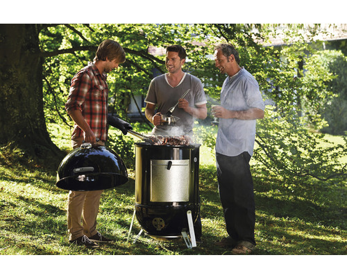 Drei Männer grillieren mit einem Holzkohlegrill im Freien.