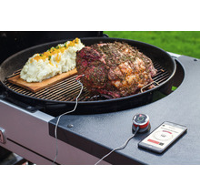Ein Braten und Kartoffelpüree auf einem Grill mit einem verbundenen Thermometer und einem Smartphone, das die Temperatur anzeigt.