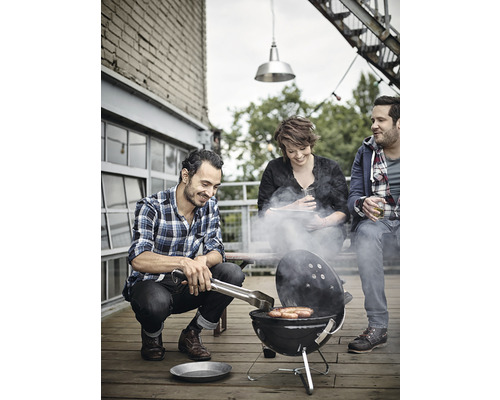 Trois personnes font griller des saucisses sur un sol en bois avec un barbecue boule.