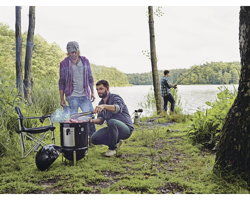 Szene mit Männern beim Grillen am See, einem Holzkohlegrill und einem Angler