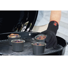 Une personne portant un gant de barbecue place des ramequins contenant des gâteaux aux myrtilles sur un gril.