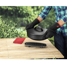 Personne avec des gants de barbecue manipule un four hollandais sur une table en bois à l''extérieur.