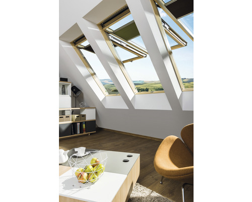 Chambre mansardée avec fenêtres de toit, meublée de manière lumineuse avec une commode, une table et un fauteuil