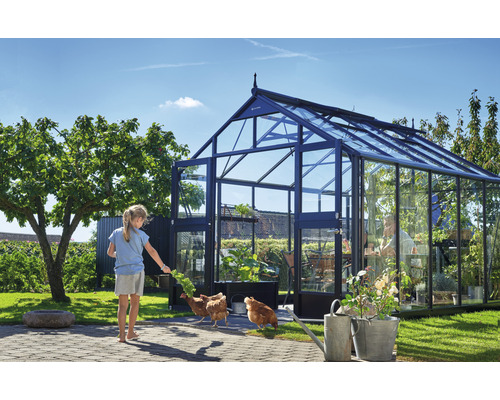 Ein Gewächshaus im Garten mit einem Kind, das Hühner füttert.