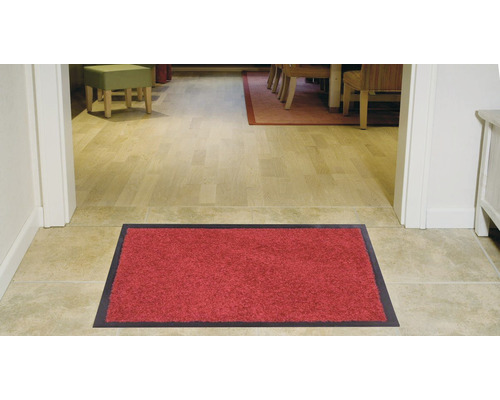 Tapis de sol rouge avec bord foncé devant une entrée de maison.