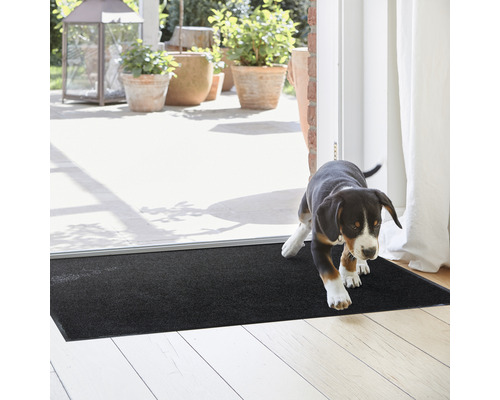 Paillasson noir devant une porte de patio avec un chiot qui se tient dessus.