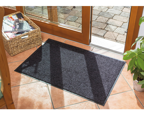 Paillasson gris devant une porte de terrasse sur un sol carrelé.