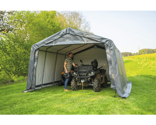 Abri gris pour appareils avec un homme et un quad sur une prairie.