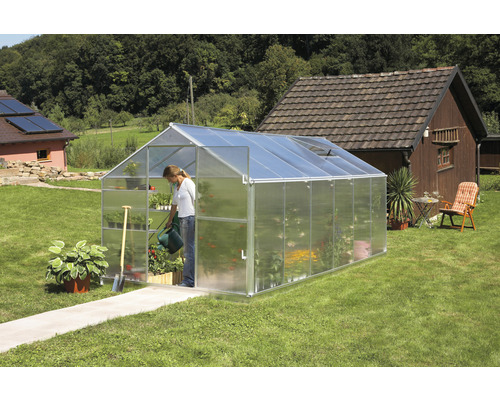 Serre dans le jardin avec une femme arrosant des plantes