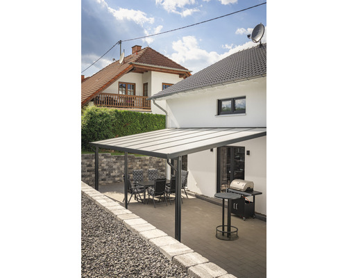 Toiture de terrasse gutta Premium acrylique transparent 712 x 306 cm anthracite Terrasse avec auvent, table de jardin, chaises et barbecue devant une maison d''habitation.