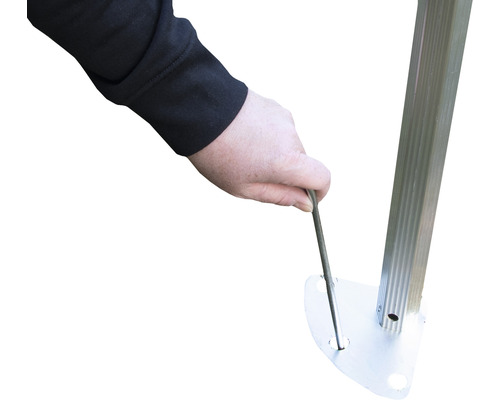 Une personne fixe un pavillon au sol avec un piquet.