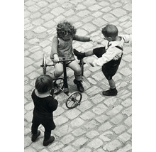 Drei Kinder spielen auf einem gepflasterten Platz, eines auf einem Dreirad, ein Rad liegt daneben.