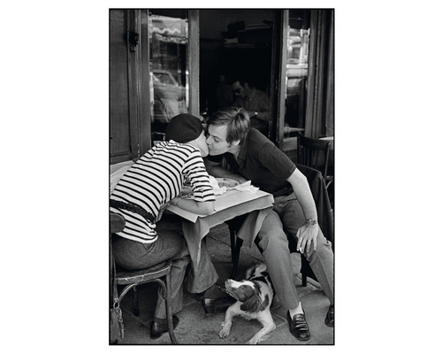 Schwarzweißfoto von einem Paar, das sich in einem Café küsst, mit einem Hund, der unter dem Tisch liegt.