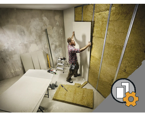 Un homme installe des plaques de plâtre sur un mur avec du matériau isolant et des profilés métalliques