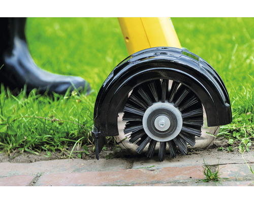 Detailaufnahme einer Fugenkratzbürste beim Einsatz im Garten zur Reinigung von Pflastersteinen