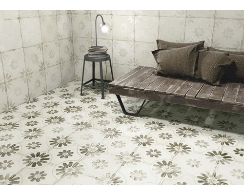 Raumansicht mit Bodenfliesen und Wandfliesen im Blumendesign, ergänzt durch eine Sitzbank, einen Hocker und eine Lampe