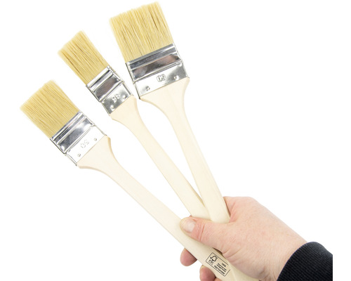 Trois pinceaux à vernis avec manche en bois dans une main