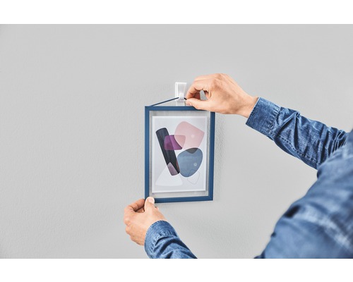 Une personne accroche une photo encadrée au mur avec des bandes adhésives