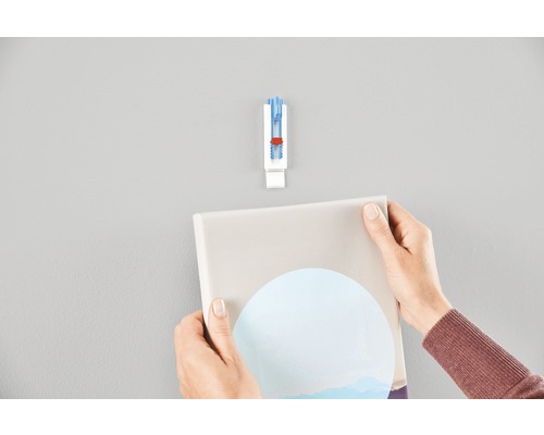 Une personne accroche une image au mur à l''aide d''un crochet d''image auto-adhésif.