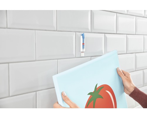 Une personne accroche une photo sur des carreaux avec une bande adhésive