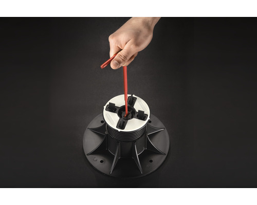 Une main ajuste un plot de terrasse avec un outil.