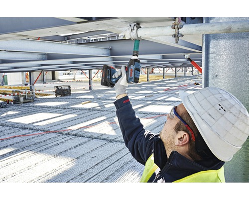 Un ouvrier du bâtiment fixe un support de tuyau à une structure métallique à l'aide d'une visseuse sans fil.
