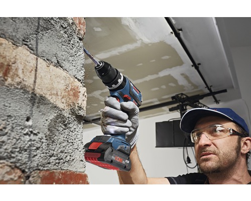 Un homme perce un mur de briques avec un perforateur sans fil.