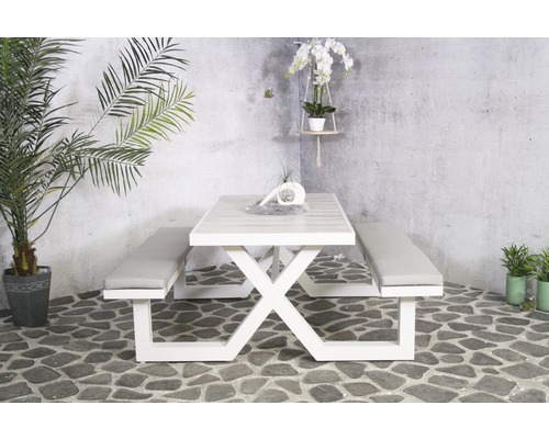 Helle Gartensitzgruppe mit Tisch und Bänken mit Polsterauflagen vor einer Betonwand