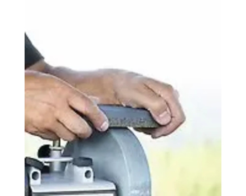 Des mains affûtent un outil à l''aide d''une meuleuse