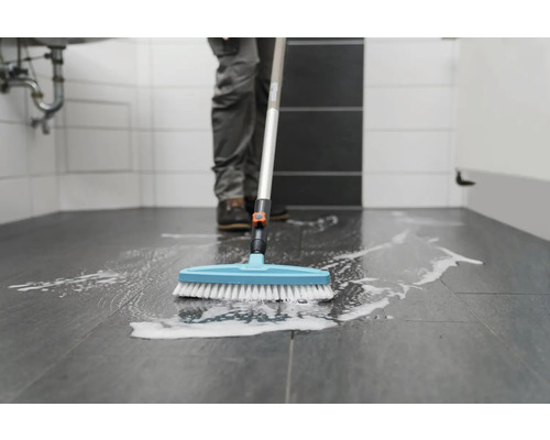 Person reinigt Badezimmerboden mit Reinigungsbürste