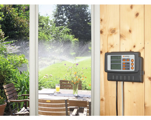 Contrôleur d''arrosage Gardena donnant sur un jardin avec arroseurs de pelouse