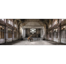 Grande salle avec scène, piano et grandes fenêtres dans un bâtiment nécessitant des rénovations.