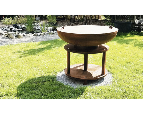 Feuerstelle aus Stahl auf Rasenfläche mit Teich im Hintergrund