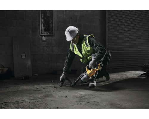 Un homme portant un casque de sécurité et un gilet de sécurité utilise un aspirateur industriel sur un sol en béton.