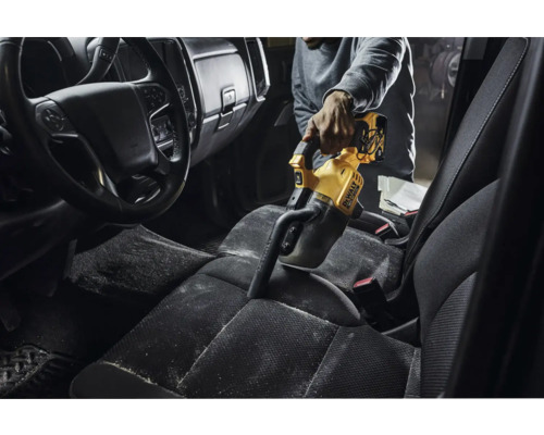 Une personne aspire l''intérieur d''une voiture avec un aspirateur à main jaune DeWalt.