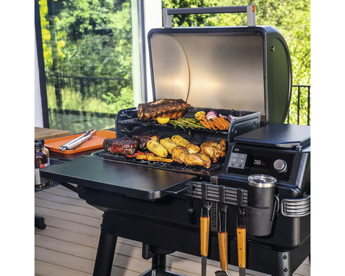 Grill avec couvercle ouvert, aliments grillés et accessoires sur la surface de cuisson.