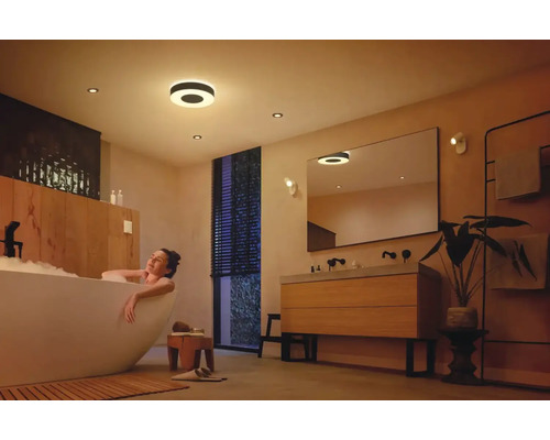 Salle de bains lumineuse avec plafonniers et femme dans la baignoire