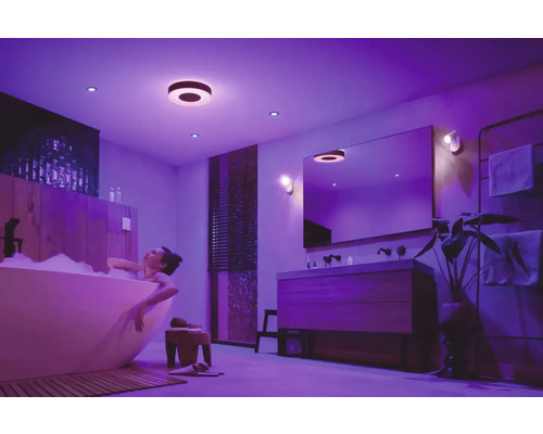 Femme se détend dans une baignoire sous des plafonniers et des spots encastrés dans une salle de bains.