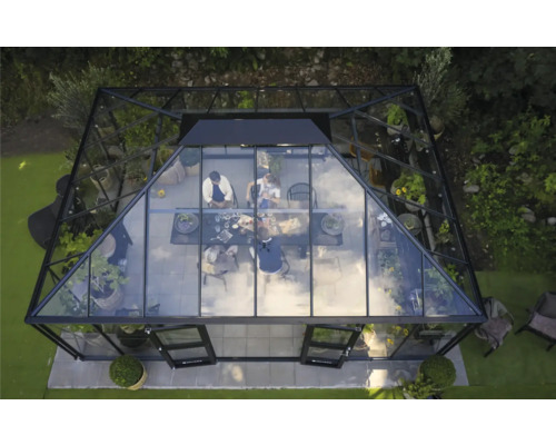 Aussenansicht eines Gewächshauses mit Pflanzen und einer Gruppe von Personen, die an einem Tisch sitzen.