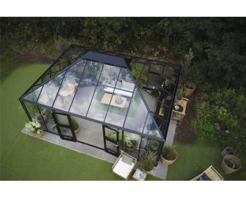 Gewächshaus mit Glaswänden und schwarzem Rahmen im Garten, eingerichtet mit Sitzmöbeln