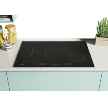Table de cuisson à induction Candy noire avec quatre zones de cuisson sur un comptoir de cuisine.