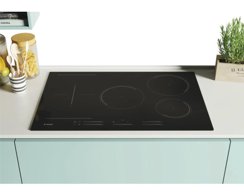 Table de cuisson à induction Candy noire avec quatre zones de cuisson sur un comptoir de cuisine.