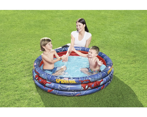 Piscine gonflable pour enfants avec motif Spiderman dans le jardin avec des enfants qui jouent et une femme.