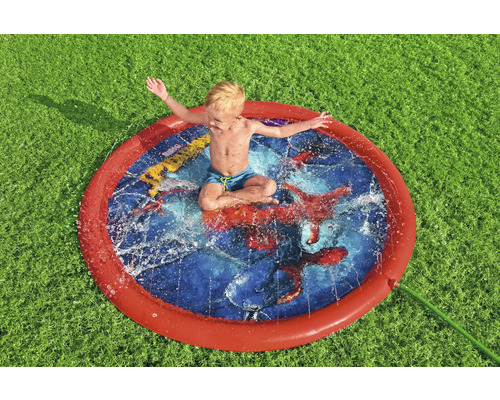 Garçon assis dans un arroseur d''eau rond sur la pelouse