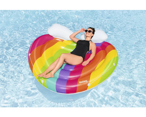 Femme se détend sur un matelas pneumatique en forme de cœur arc-en-ciel dans l''eau.
