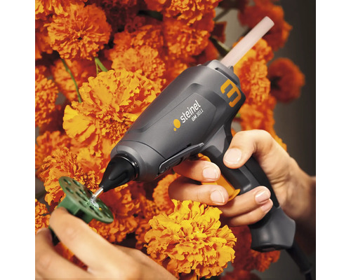 Pistolet à colle chaude Steinel collant une pièce à l''aide de colle thermofusible sur fond de fleurs orange.
