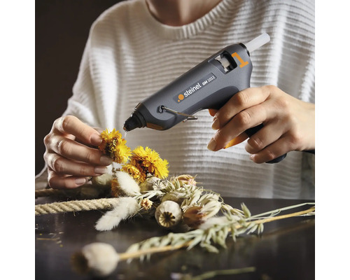 Anwender fixiert mit Heissklebepistole Blüten auf einem Kranz