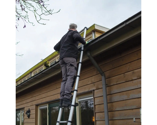 Un homme nettoie une gouttière avec une échelle télescopique sur une maison.