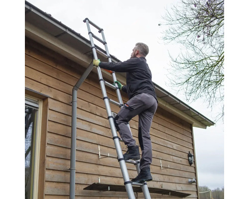 Une personne monte à une échelle télescopique contre un mur de maison.